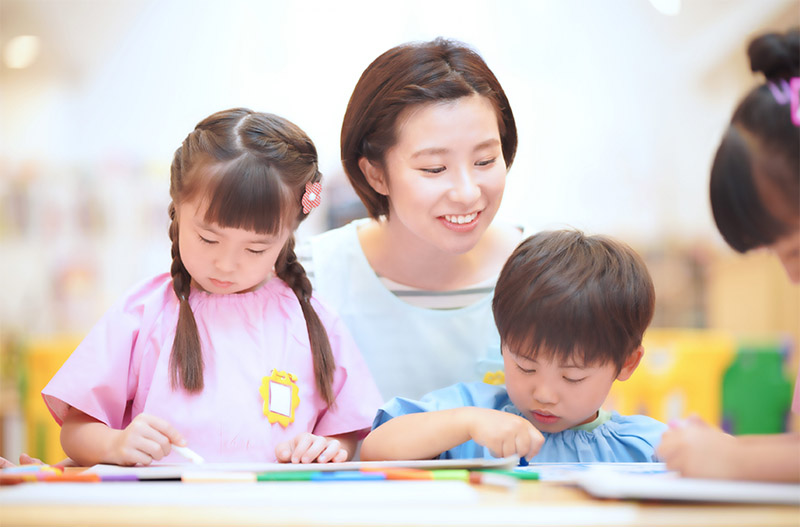 園児と絵を描く幼稚園の先生